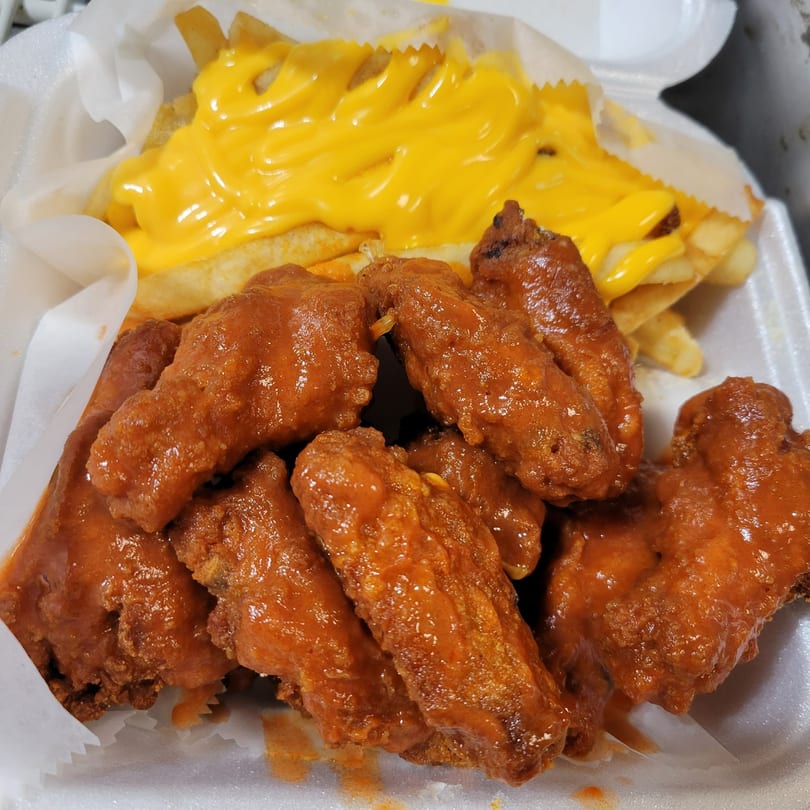 Hooks Fish & Chicken Plus's buffalo wings and cheese fries in a white takeout container.